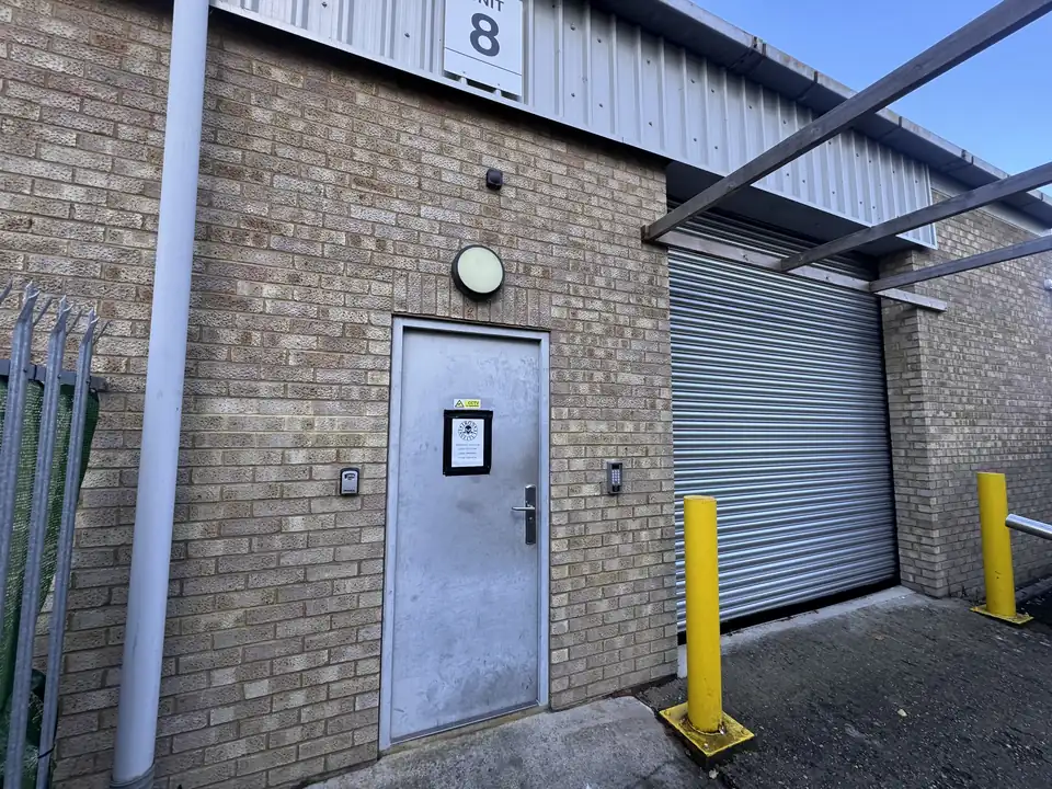 The grey entrance door to Iron Institute on Hollands Road, with the gym's logo on the door, a key fob reader beside it and yellow bollards by the roller shutter